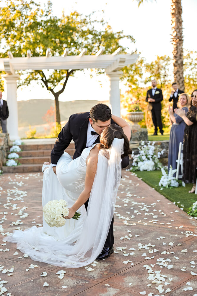 A groom dipping his bride for a kiss as the wedding party cheers
