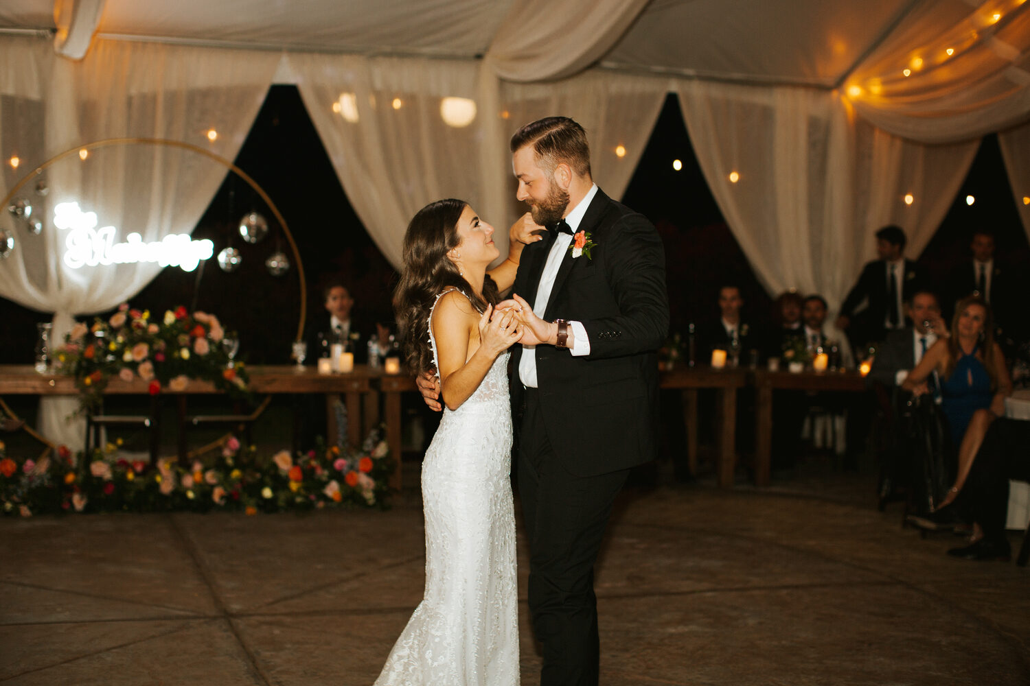 A couple's first dance under warm lights in the reception tent